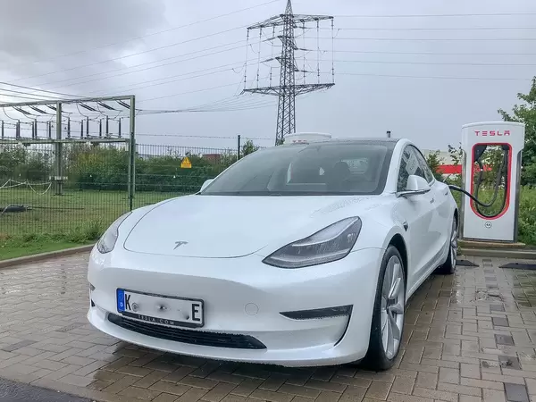 E-Mobilität: Weißer Tesla Model 3 lädt an einer Supercharger - Ladesäule bei Regenwetter