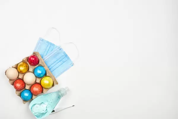 Easter and Covid-19: dyed eggs in a carton, hand sanitizer, thermometer, face masks and copy space