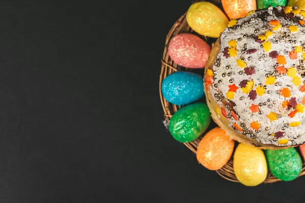 Easter cake and colorful eggs on black, top view