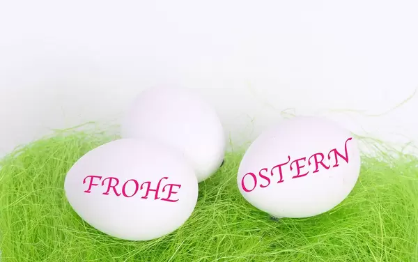 Easter eggs on green grass with Frohe Ostern text