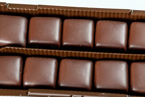 Eckige Süßigkeiten mit Schokoladenglasur in Kunststoffverpackung vor weißem Hintergrund