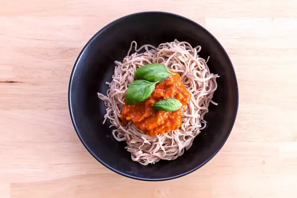 Edamama Bio-Spaghetti aus Azuki Bohnen mit Tomatensauce und Basilikumblättern auf schwarzem Teller