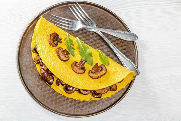Egg omelet with mushrooms and arugula leaves and forks. Top view