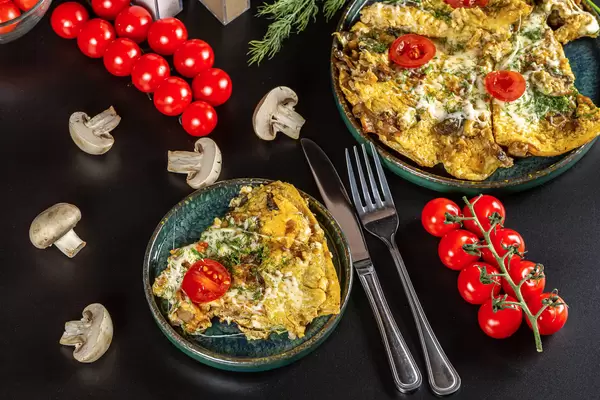 Egg omelet with mushrooms, cheese, tomatoes and herbs on a dark background