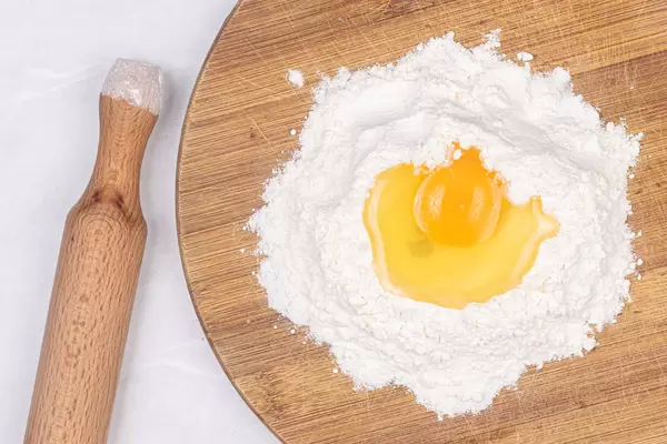 Egg on the top of the flour with wooden rolling pin