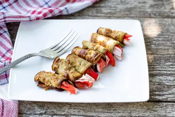 Eggplant rolls and crab sticks on a white plate with a fork