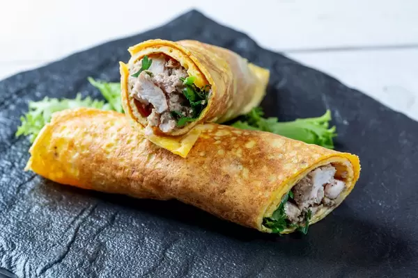 Eieromelette gefüllt mit Fleisch und Kräutern schön angerichtet auf Schieferplatte