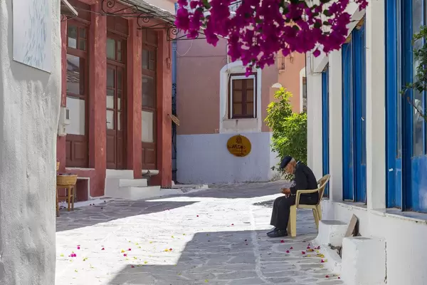 Ein alter Mann sitzt alleine in einer bunten Gasse von Chalki, Örtchen im zentralen Hochland von Naxos