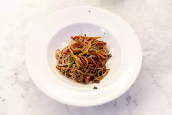 Ein asiatisches Nudelgericht mit Paprikastreifen auf einem tiefen weißen Teller mit breitem Rand