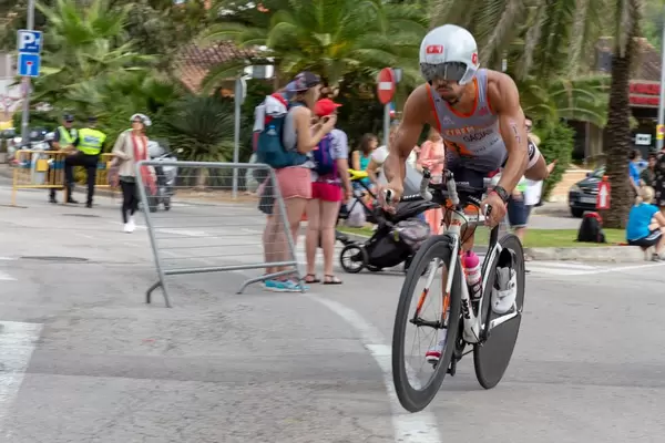Ein Athlet mir Bart und weißem Helm schwingt sich auf das Rennrad bei einem Triathlon