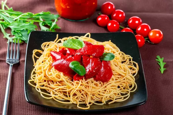 Ein Berg Spaghetti mit geschälten Tomaten und Basilikumblättern auf einem schwarzen Teller