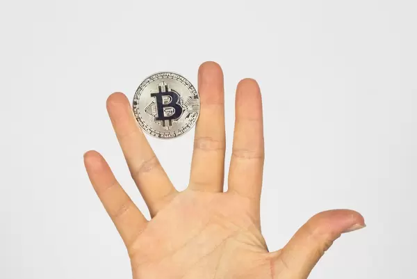 Ein Bitcoin zwischen den Fingern einer Hand