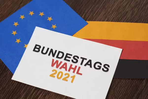 Ein Blatt mit Schrift "Bundestagswahl 2021" in den deutschen Farben, europäische und deutsche Flagge