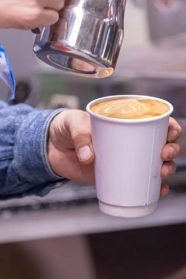 Ein Cappuccino im Pappbecher wird zubereitet