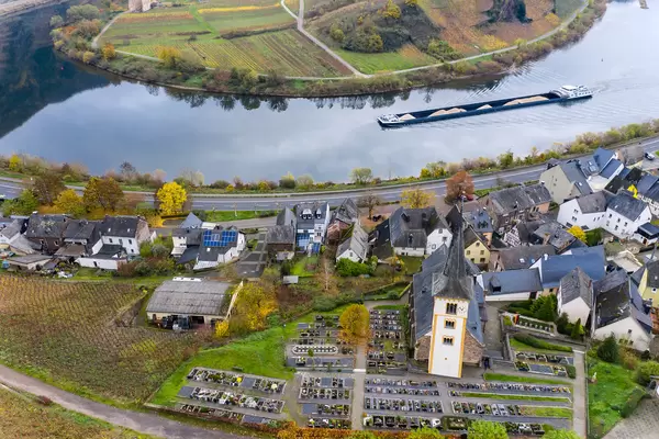Ein Frachtschiff mit Sand beladen fährt im Fluss Mosel entlang der Bundesstraße B49 in Bremm, Deutschland mit Blick auf die St. Laurentius Kirche Drohnenaufnahme