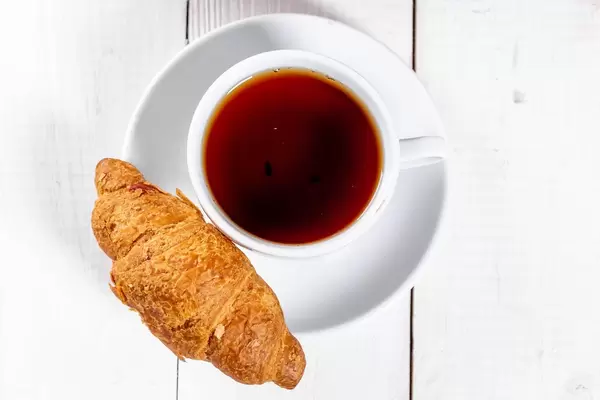 Ein frisches Croissant mit einer Tasse schwarzem Tee