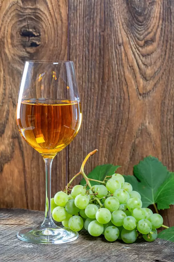 Ein gefülltes Glas Wein und Weintrauben vor einem rustikalen Holzhintergrund