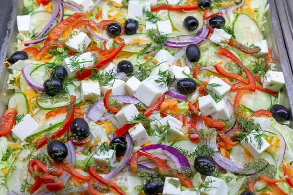 Ein gemischter Salat mit Gurken, Paprika, Zwiebeln, schwarzen Oliven, geriebenen Karotten und Feta Käse