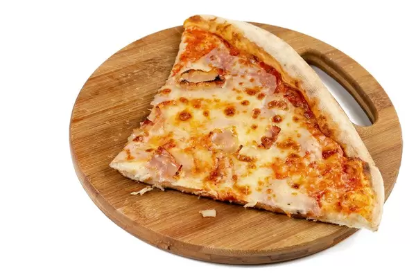 Ein gevierteltes Pizzastück mit Schinken auf rundem Holzteller vor weißem Hinterrgund