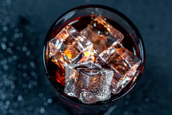 Ein Glas Cola mit Eiswürfeln in einem Gas in der Aufsicht auf schwarzem Hintergrund