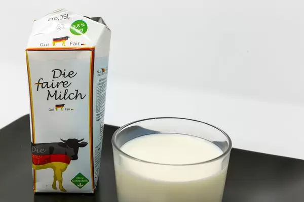 Ein Glas faire Deutsche Vollmilch - Ohne Gentechnik  - Nahaufnahme - mit Verpackung auf schwarzem Teller