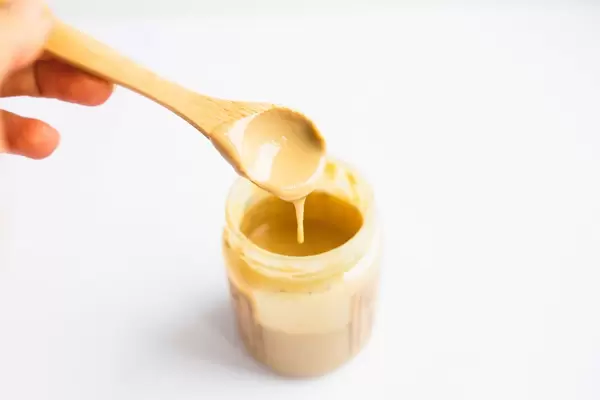 Ein Glas geschmolzene Erdnussbutter mit einem Holzlöffel auf weißem Hintergrund