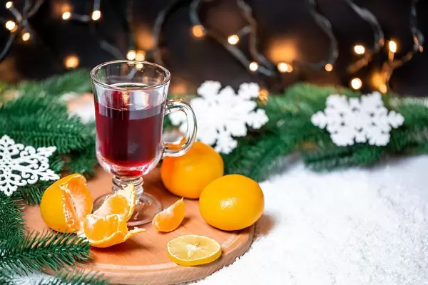 Ein Glas Glühwein mit Mandarinen und Tannenzweigen im Schnee
