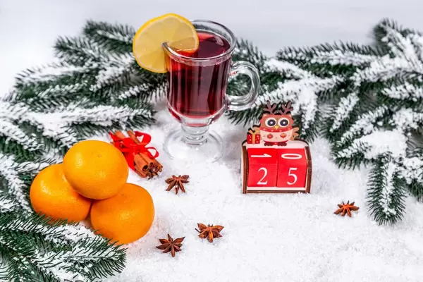 Ein Glas Glühwein zwischen Tannenzweigen, Orangen, Zimt im Schnee