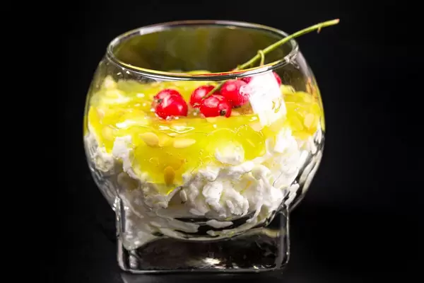 Ein Glas Hüttenkäse-Dessert mit frischer Kiwanofrucht und Johannisbeeren vor schwarzem Hintergrund