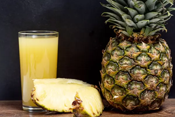Ein Glas mit frischem Ananas Saft neben einer reifen Ananas in der Nahaufnahme