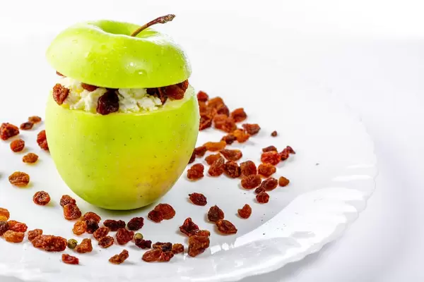Ein grüner Apfel, gefüllt mit Hüttenkäse und Rosinen als gesunder Nachtisch