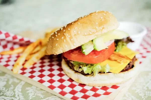 Ein halb geöffneter Cheeseburger mit Pommes im Hintergrund auf kariertem Papier