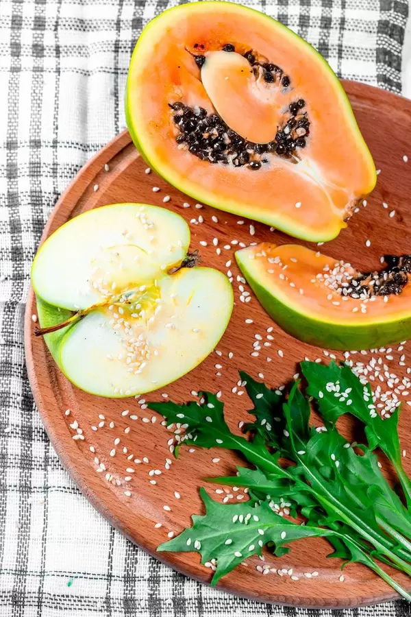 Ein halbes Apple ein Stück Papaya-Rucola und Sesam auf einem Holzbrett