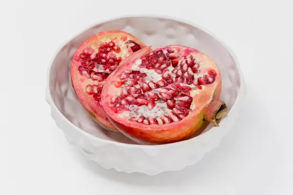 Ein halbierter Granatapfel in weißer Schale auf weißem Hintergrund