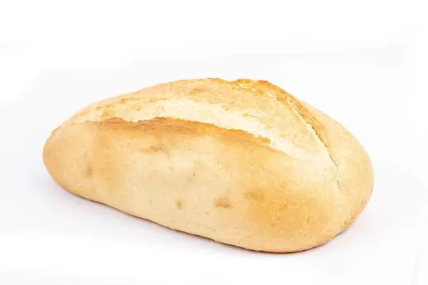 Ein helles, ganzes Weißbrot am Stück liegt auf einer weißen Oberfläche