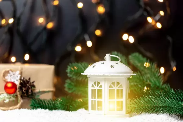 Ein Kerzenlicht im Schnee mit Tannzweigen vor dunklem Hintergrund in dem Lichter funkeln