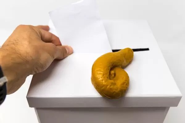 Ein Kothaufen / Scheisshaufen liegt auf einer Wahlurne, während ein Mann seinen Stimmzettel abgibt