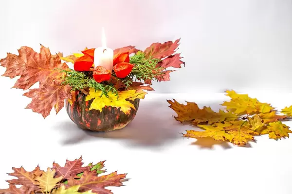 Ein Kürbis mit bunten Herbstblättern, Physalis und leuchtender Kerze auf weißem Hintergrund