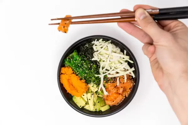 Ein Mann entnimmt mit Essstäbchen ein Stück Lachs aus der Poke Teriyaki Lachs Bowl