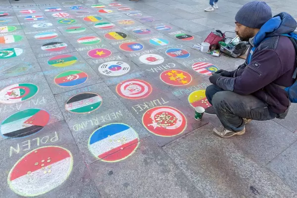 Ein Mann sammelt Spenden mit auf dem Boden des Kölner Weihnachtsmarkts gemalte Länderflaggen