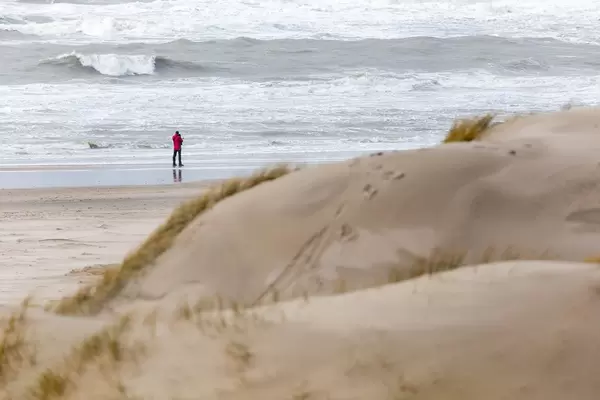 Ein Mann spaziert am Strand, Sanddünen im Vordergrund