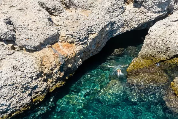 Ein Mann taucht im klaren, grünen Wasser in die Höhle Bekiri auf Spetses, Griechenland