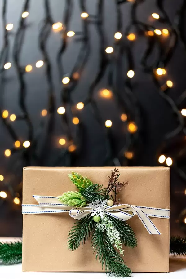 Ein mit Tannenzweigen und Zapfen verziertes Weihnachtsgeschenk in Naturpapier vor beleuchtetem Hintergrund