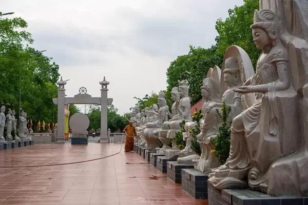 Ein Mönch wässert Pflanzen auf einem Platz mit verschiedenen Lady Buddha Statuen bei der Truc Lam Phuong Nam Pagode in Can Tho, Vietnam