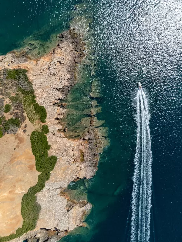 Ein Motorboot fährt an der rauen Küstenlinie der kleinen rötlichen Insel Kokkinonisi entlang