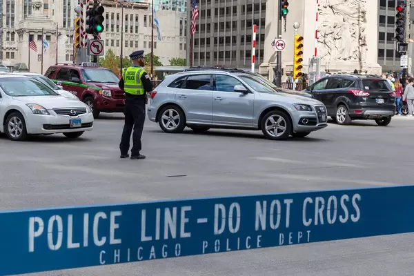 Ein Polizist steht mitten im Straßenverkehr in Downtown Chicago, während ein Bereich ist von einer blauen Barriere mit dem Schriftzug "Police line - Do not cross" abgesperrt