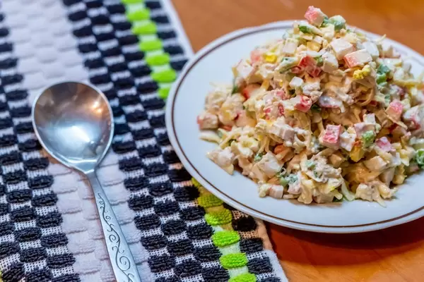Ein Salat mit Käse, Fleisch und Krebsfleisch auf einem Teller mit einem Löffel