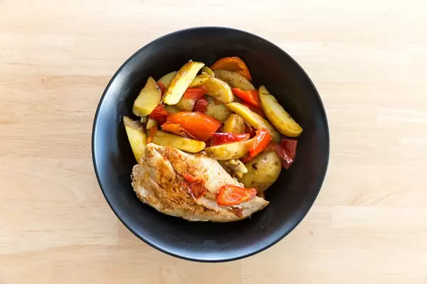 Ein schwarzer Teller mit Hähnchenbrust, Kartoffeln und roter Paprika in der Nahaufnahme