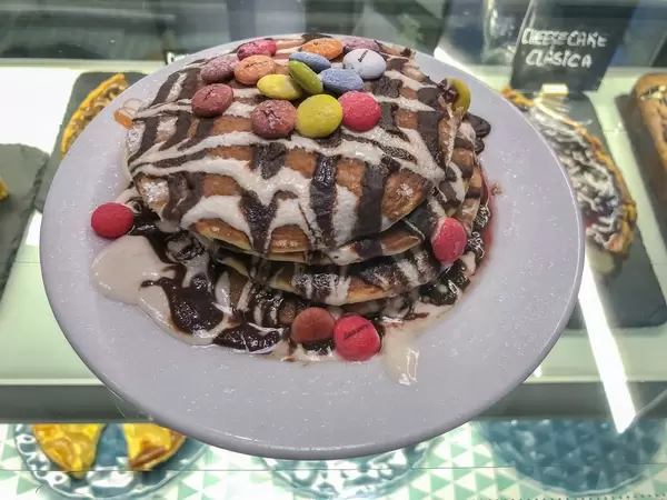 Ein Stapel Pancakes mit Smarties und Schokoladensauce auf einem weißen Tellelr