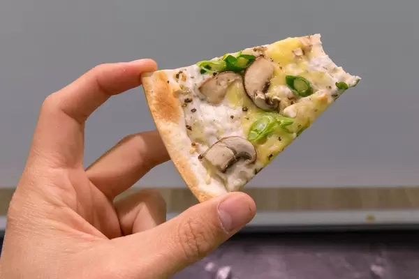 Ein Stück Flammkuchen mit Pilzen, Frühlingszwiebeln und veganem Bedda Käse